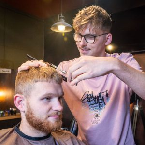 Male barber giving a male client with a beard a haircut.