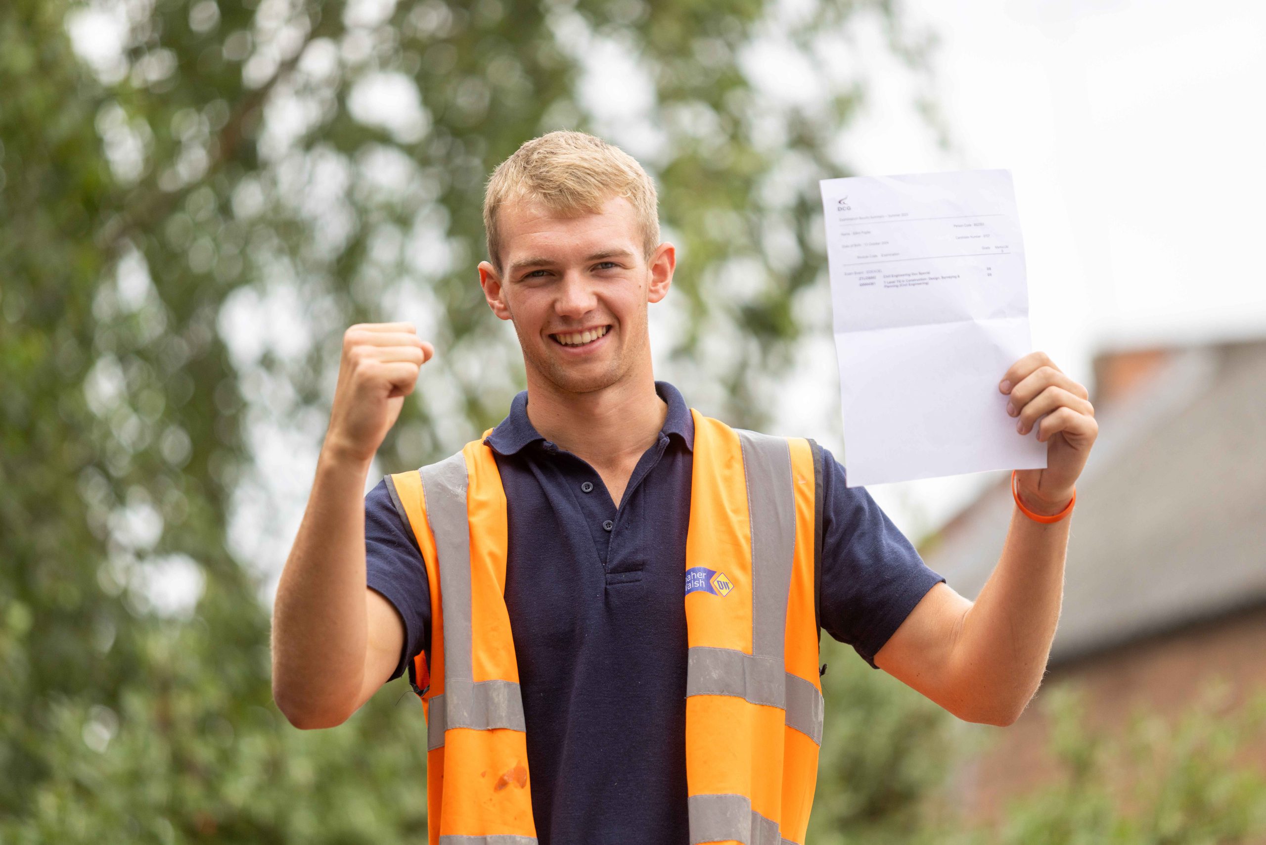 Young male with blonde hair wearing an orange hi-viz vest and holding a document with exam results on.